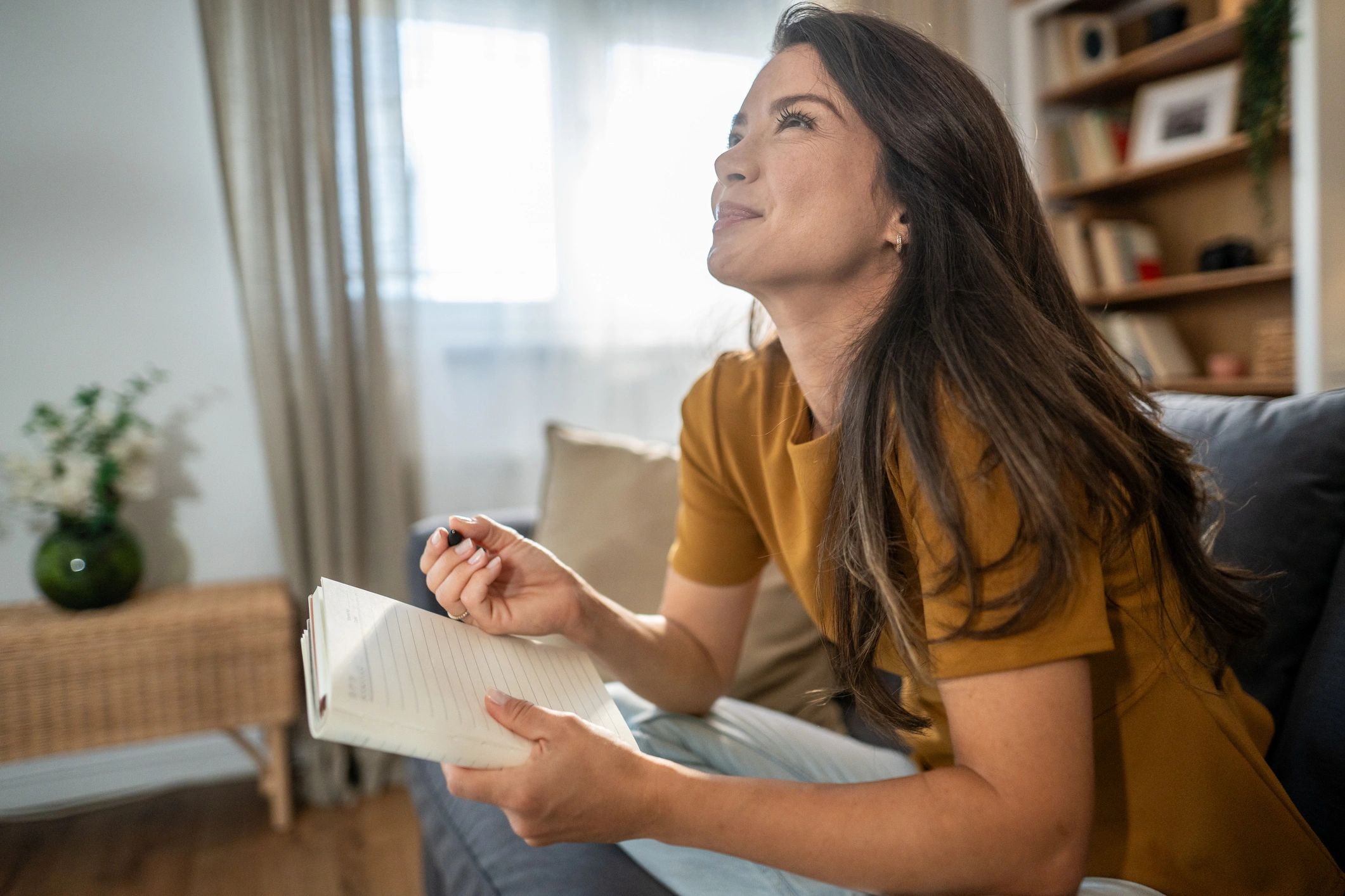 Woman journaling in a sunlit living room, reflecting and writing notes